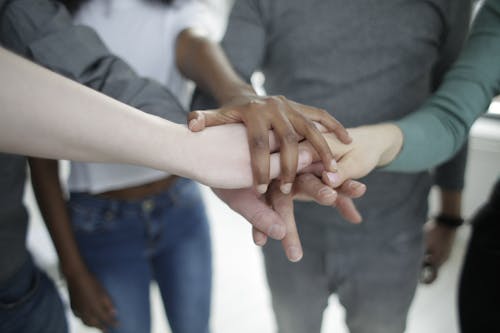 Crop diverse colleagues stacking hands together during training in office