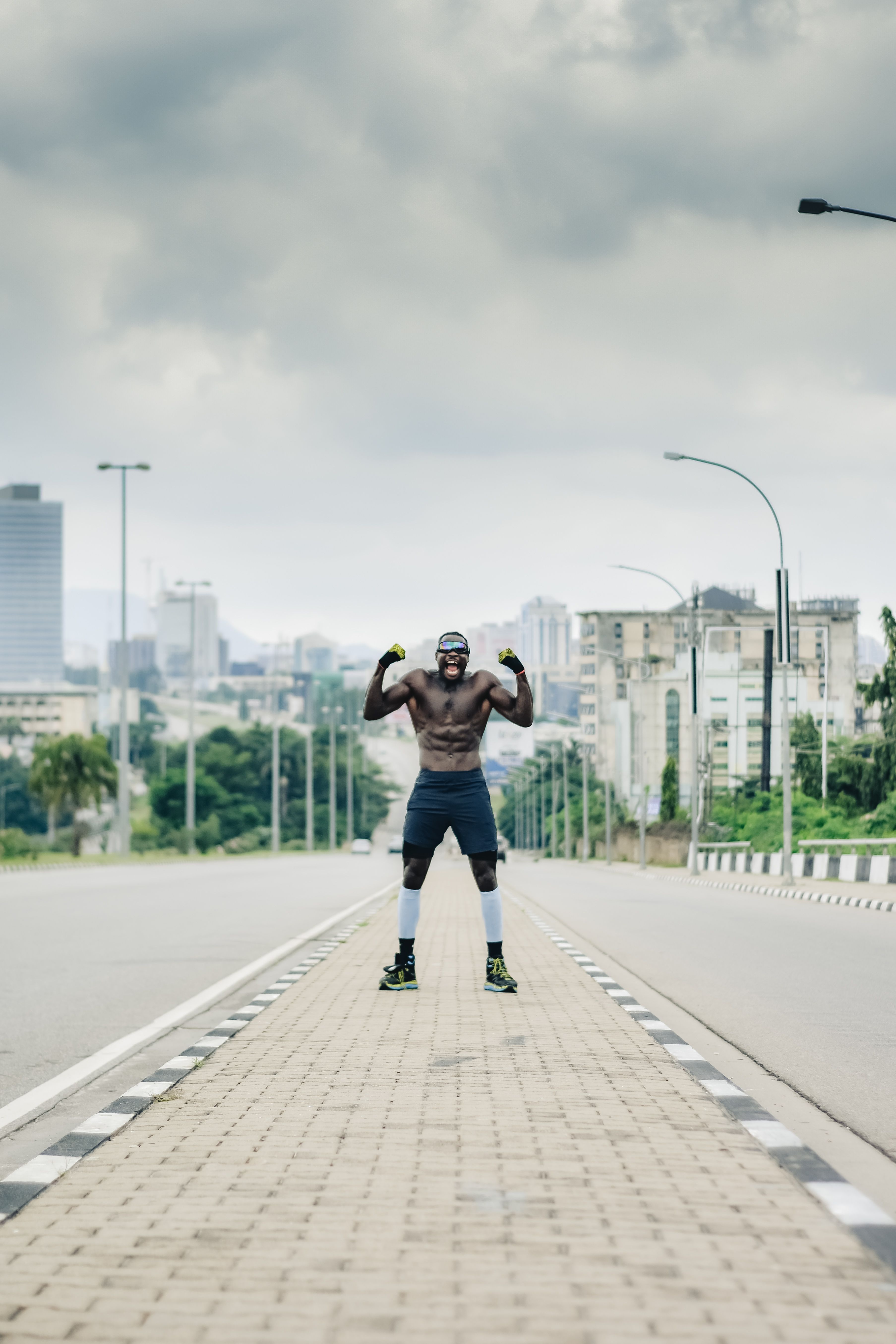 A muscular man poses confidently on an empty street in Abuja, Nigeria, showcasing strength and urban backdrop.