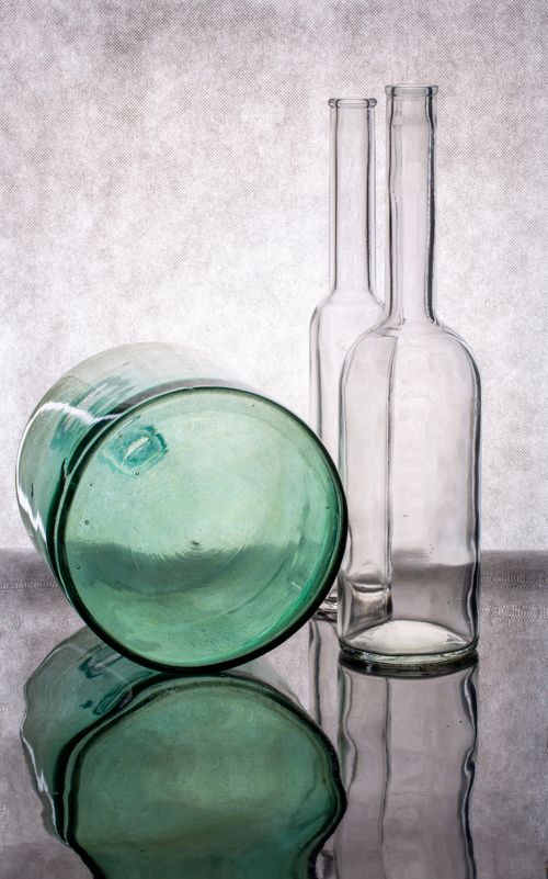 Free Two clear bottles and one green bottle creatively arranged on a reflective surface, enhancing their artistic look. Stock Photo