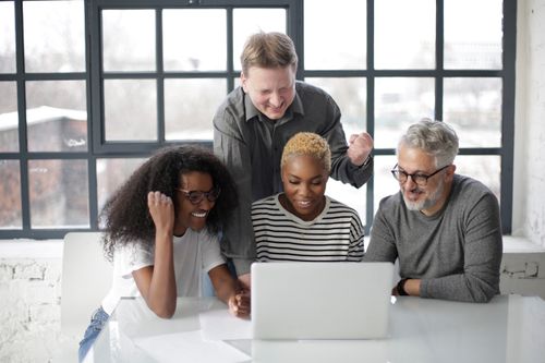 Free Happy diverse coworkers in casual clothes laughing and clenching fists celebrating end of project using laptop in light office Stock Photo