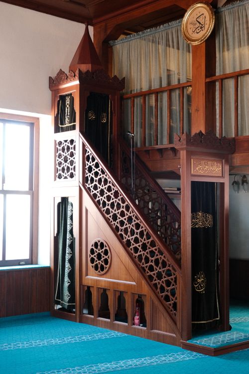 Free Beautifully detailed carved wooden minbar inside a mosque with teal carpets and Arabic inscriptions. Stock Photo