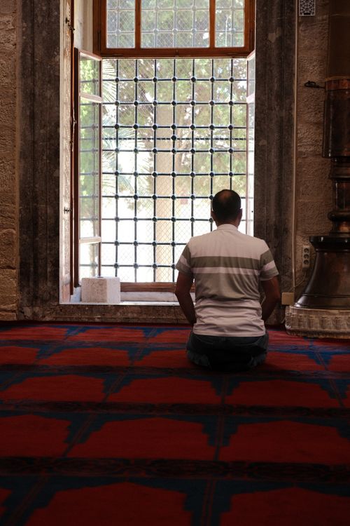 Free A man seated in prayer inside a mosque, facing a window. Stock Photo