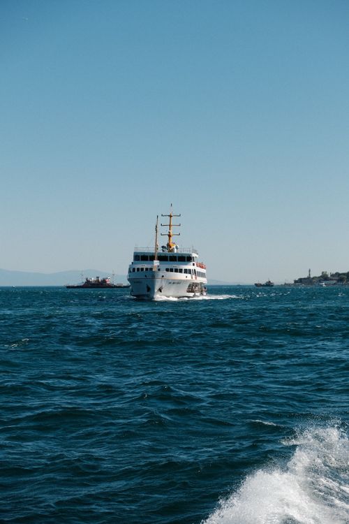 Free A white ferry boat sails through blue waters under a clear sky, near a coastal town. Stock Photo