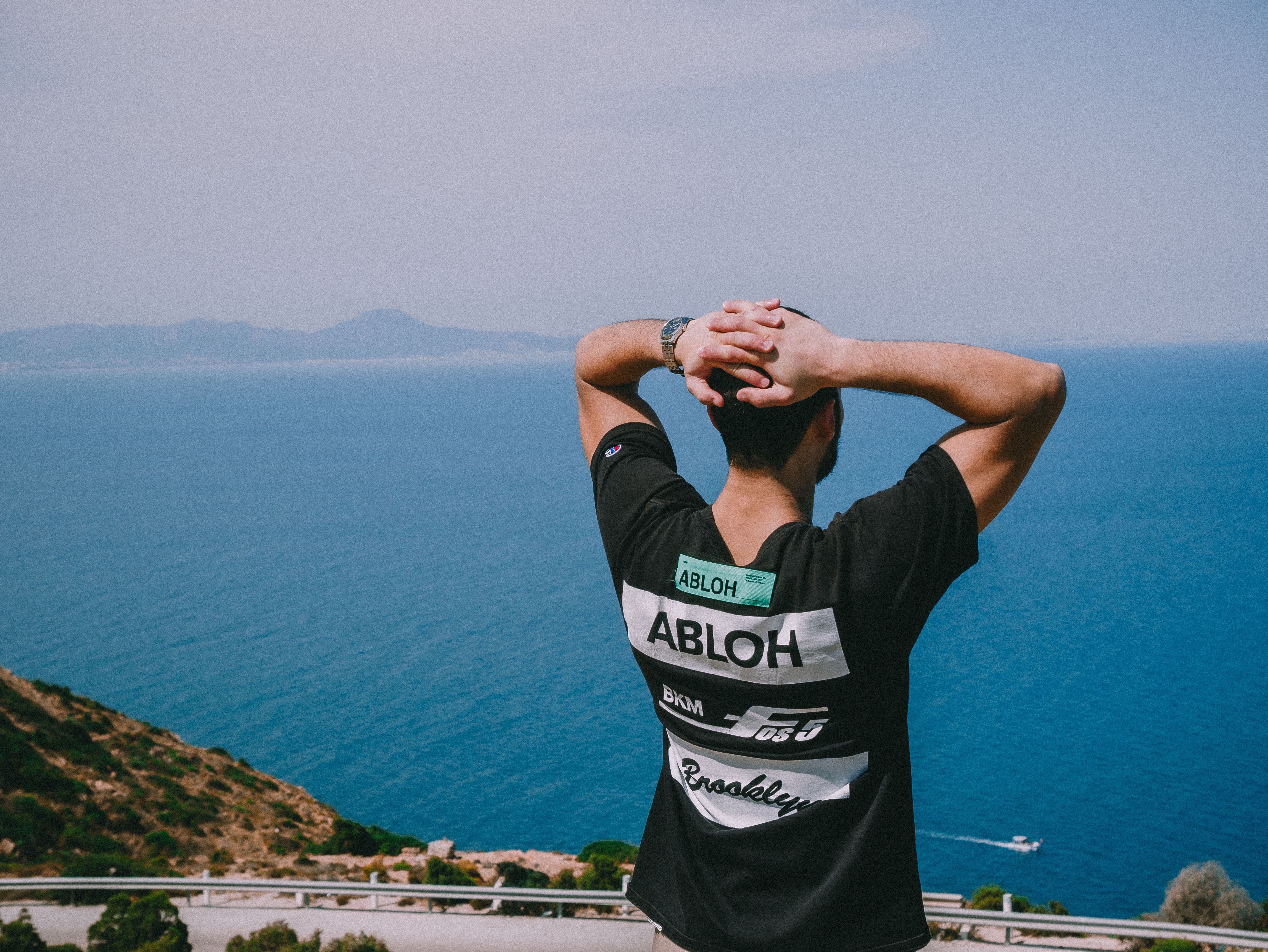 A man stands with hands on head overlooking the ocean at Qurbus, Tunisia, enjoying the serene view.