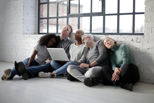 Tired multiethnic people in casual clothes with laptop sleeping while sitting on floor and leaning on each other