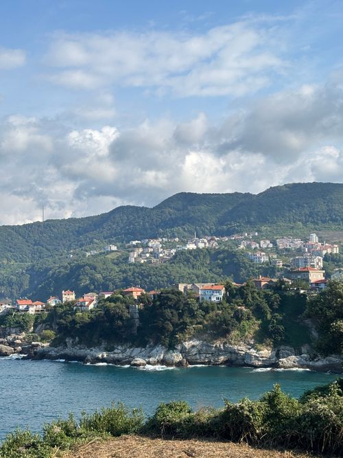 Free Picturesque coastal village with lush green mountains and blue sea under a cloudy sky. Stock Photo