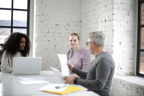 Free Cheerful group of diverse people sitting at table while old man checking documents and young colleagues working on laptop Stock Photo