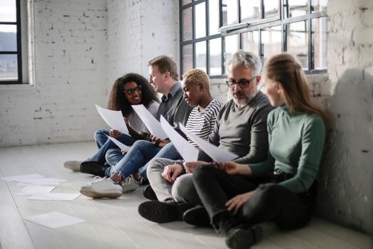 A diverse group of adults discussing paperwork in a modern, light-filled office.