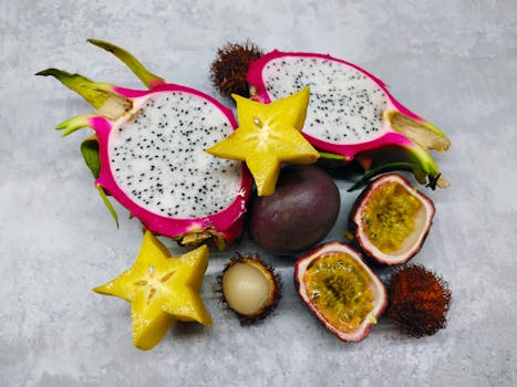 A colorful assortment of tropical fruits including dragon fruit, starfruit, passionfruit, and rambutan on a textured surface.