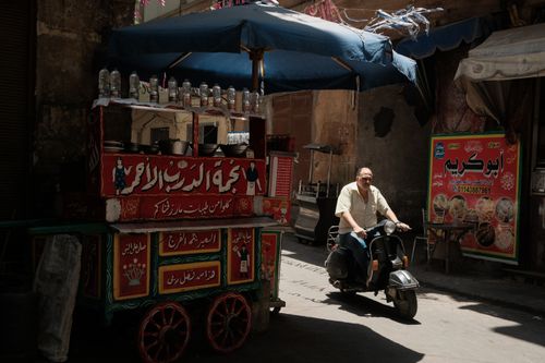 Free Traditional Egyptian street food cart with a man riding a scooter in Cairo's vibrant alley. Stock Photo