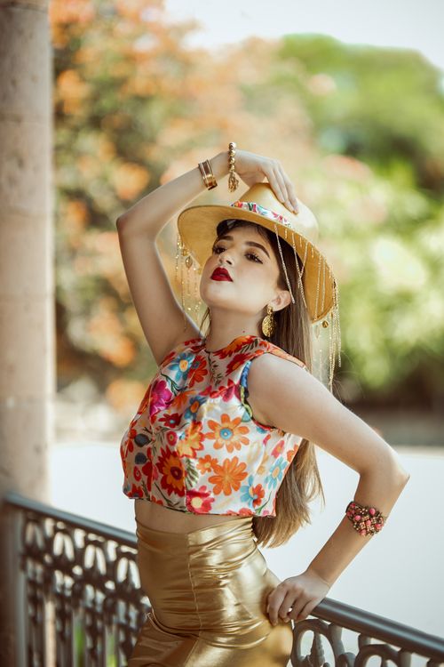 Free Stylish woman in vibrant floral outfit and boater hat poses outdoors, exuding elegance. Stock Photo