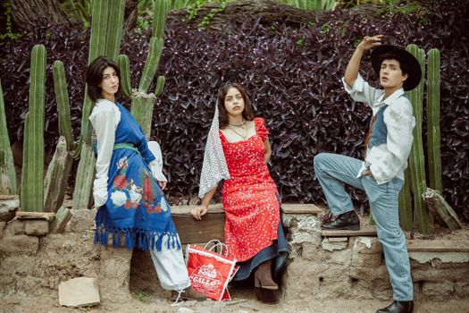 Three young adults in traditional Mexican clothing pose amidst cactus plants in León de los Aldama.