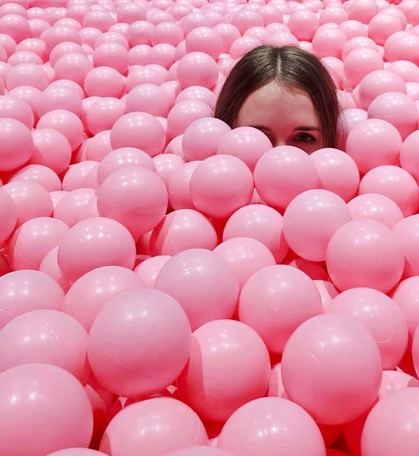 A young woman peeks through a sea of pink balls, creating a playful and lighthearted scene.