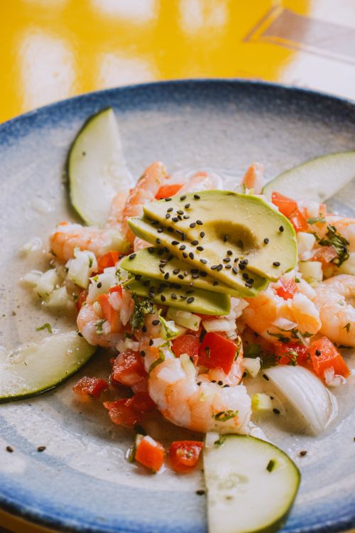 Free Delicious shrimp and avocado salad garnished with cucumbers and sesame seeds on a blue ceramic plate. Stock Photo