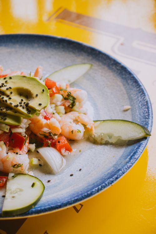 Free A vibrant platter of shrimp ceviche garnished with avocado, cucumbers, and sesame seeds on a blue plate. Stock Photo