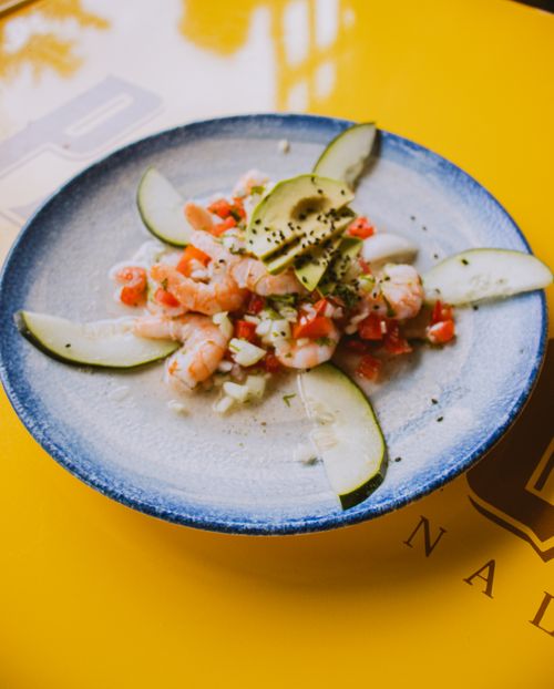 Free A beautifully plated shrimp and vegetable dish with avocado on a colorful yellow table. Stock Photo