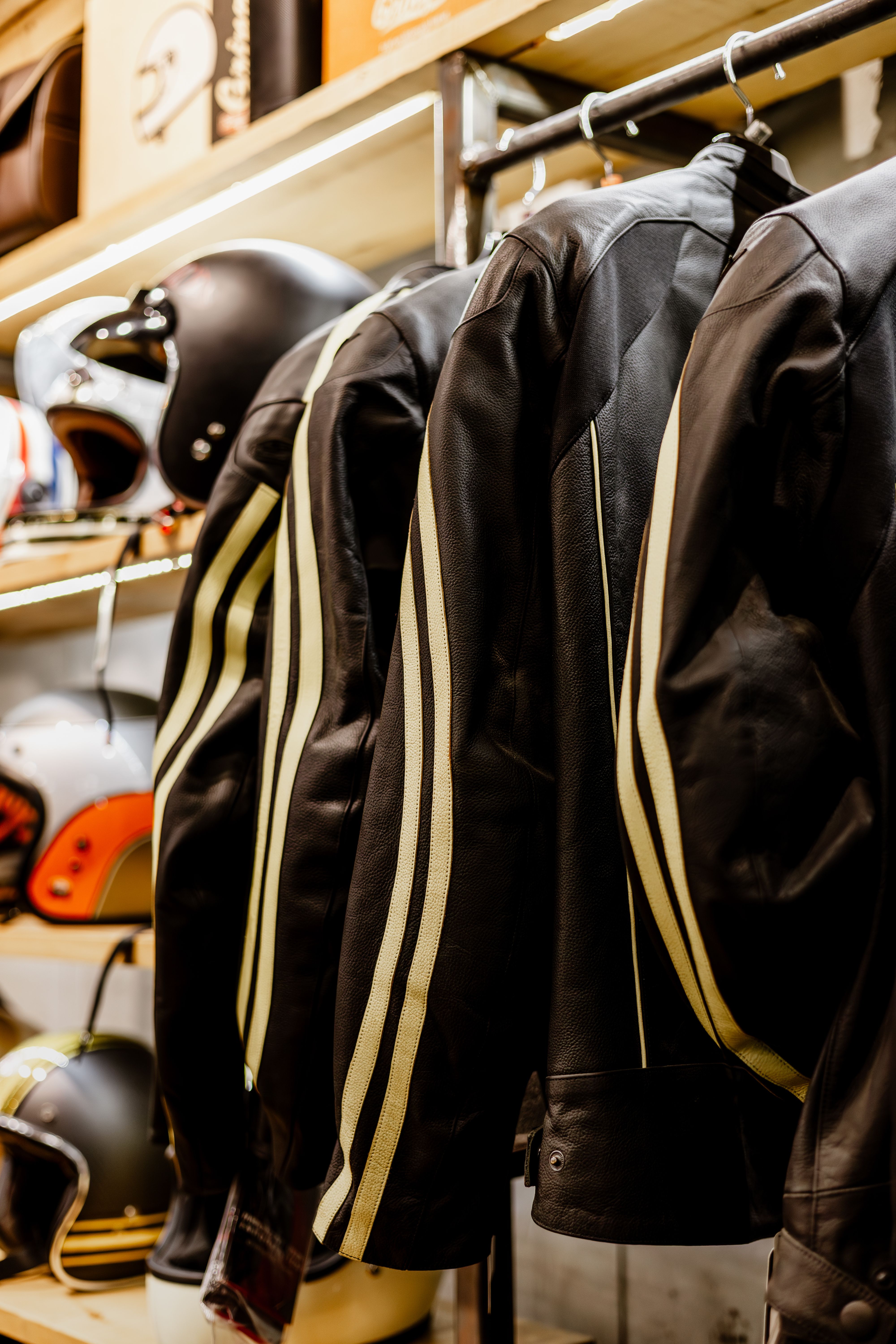 Row of classic black leather motorcycle jackets and helmets in a retail store display.