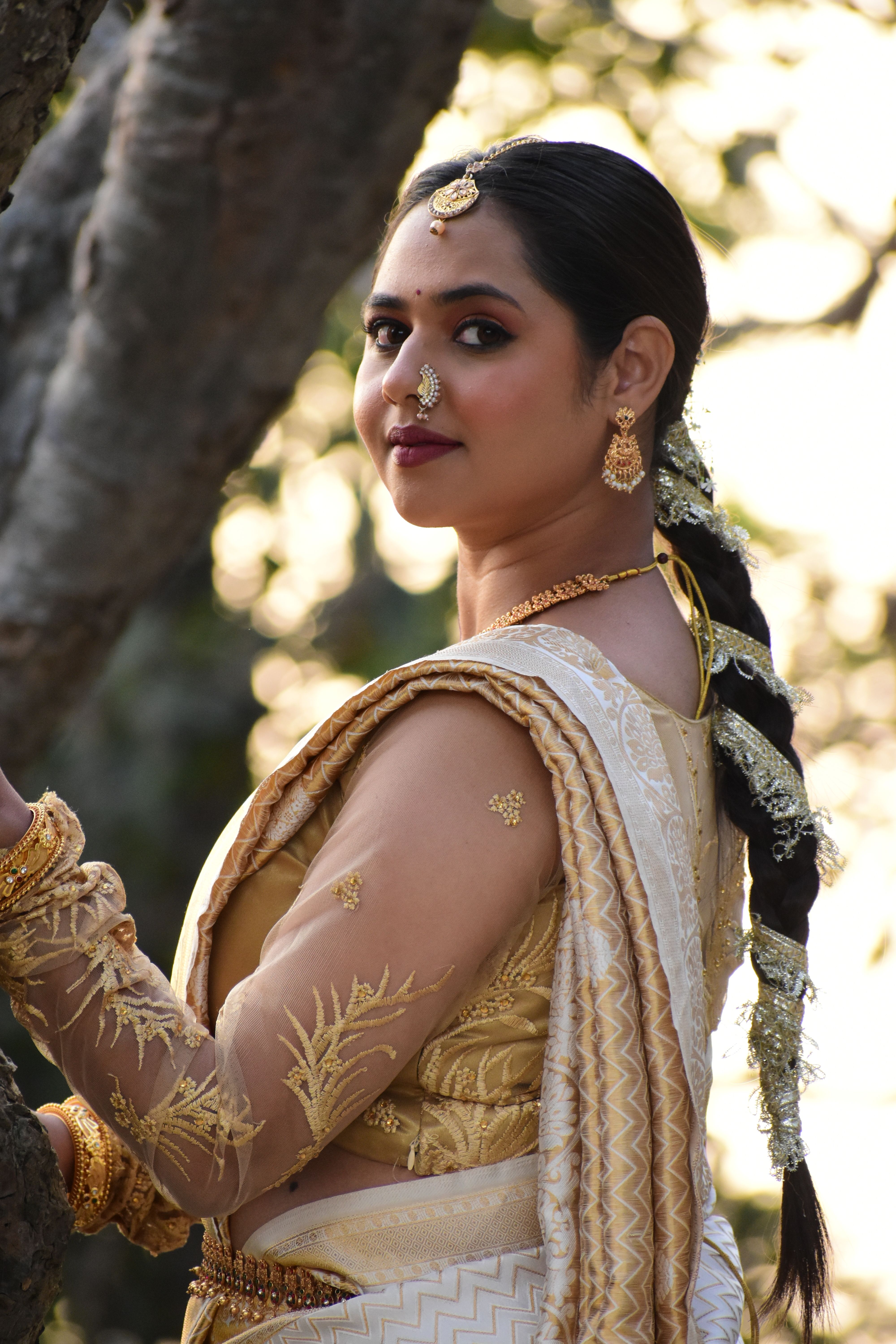 A woman in traditional Indian attire poses gracefully in a natural setting.