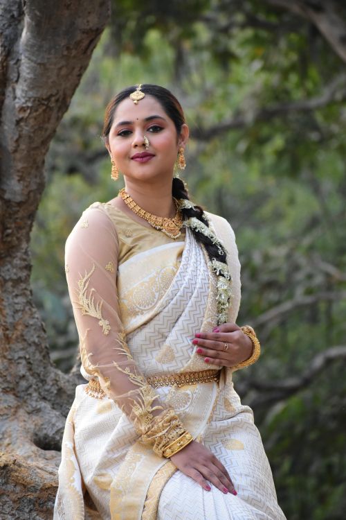 Free Beautiful Indian woman in a golden saree poses gracefully outdoors, showcasing traditional attire and jewelry. Stock Photo