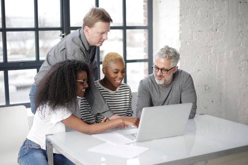 Free Happy multiethnic colleagues typing on laptop while smiling and working on business creative project against big window Stock Photo