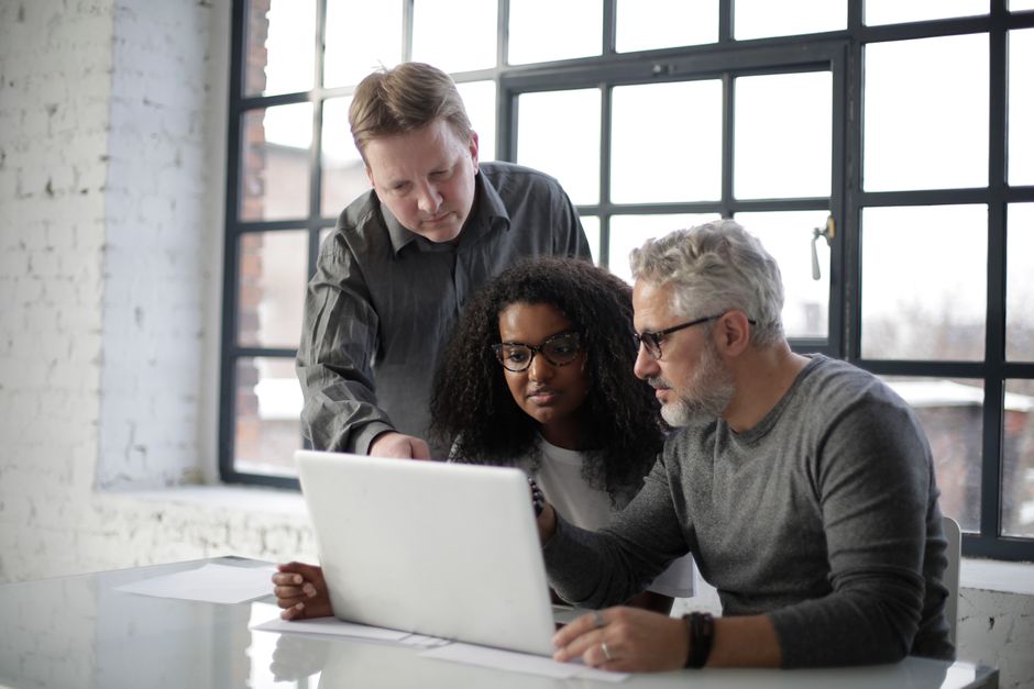 Serious multiethnic coworkers gathering at table for working on laptop and taking about details of project in daylight