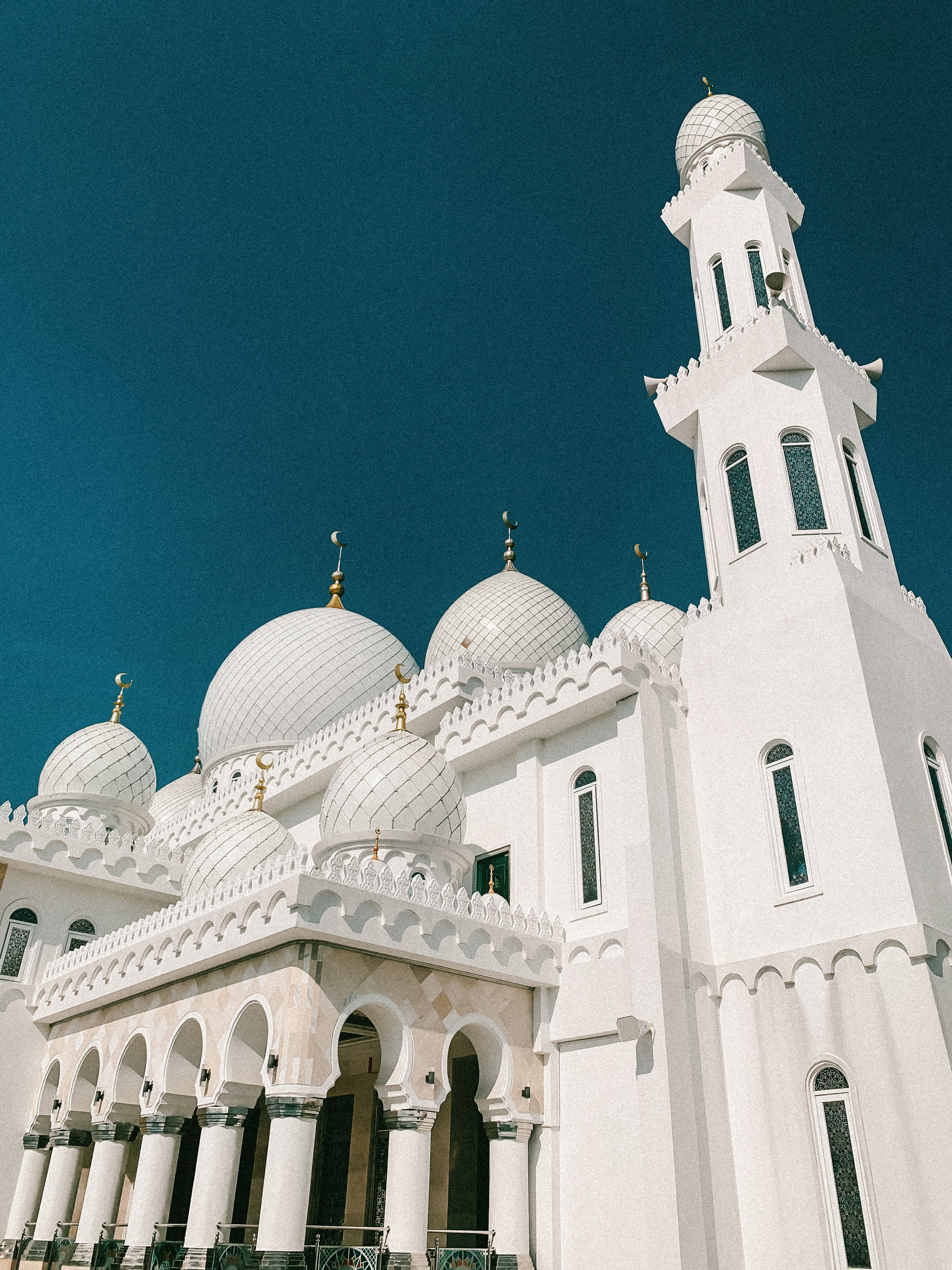 Stunning view of a white mosque with domes and minaret against a clear blue sky.