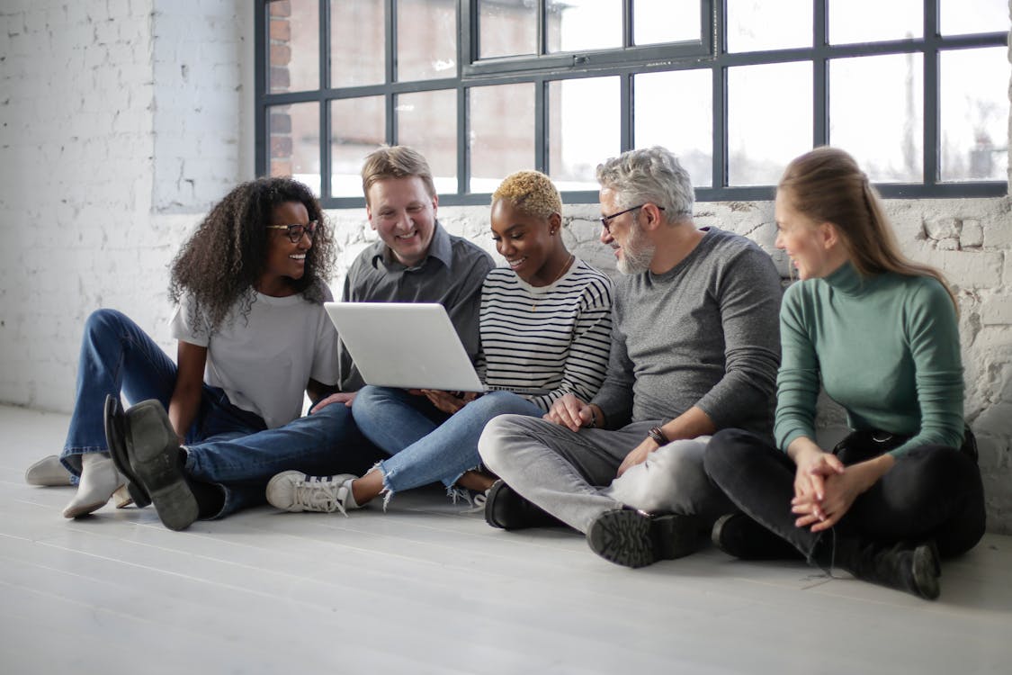 Cheerful multiracial colleagues with laptop sitting on floor