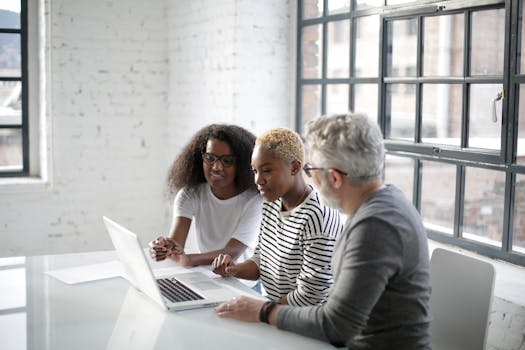Side view of black women and old gray haired man sitting at table and surfing laptop while working on creative project