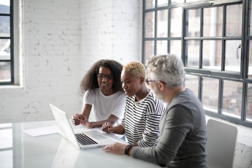 Free Side view of black women and old gray haired man sitting at table and surfing laptop while working on creative project Stock Photo