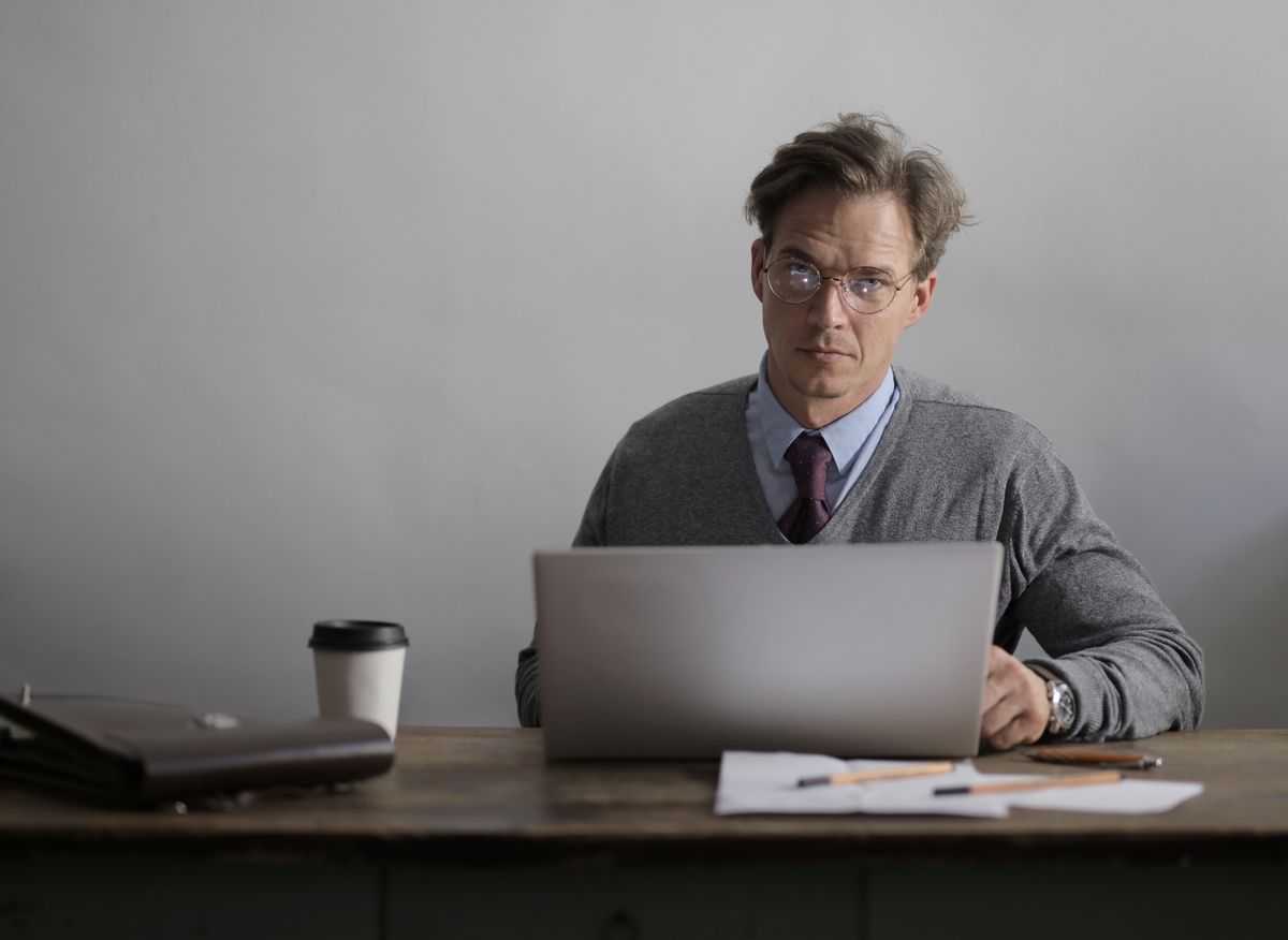 A student thinking over coffee while building a presentation on a laptop