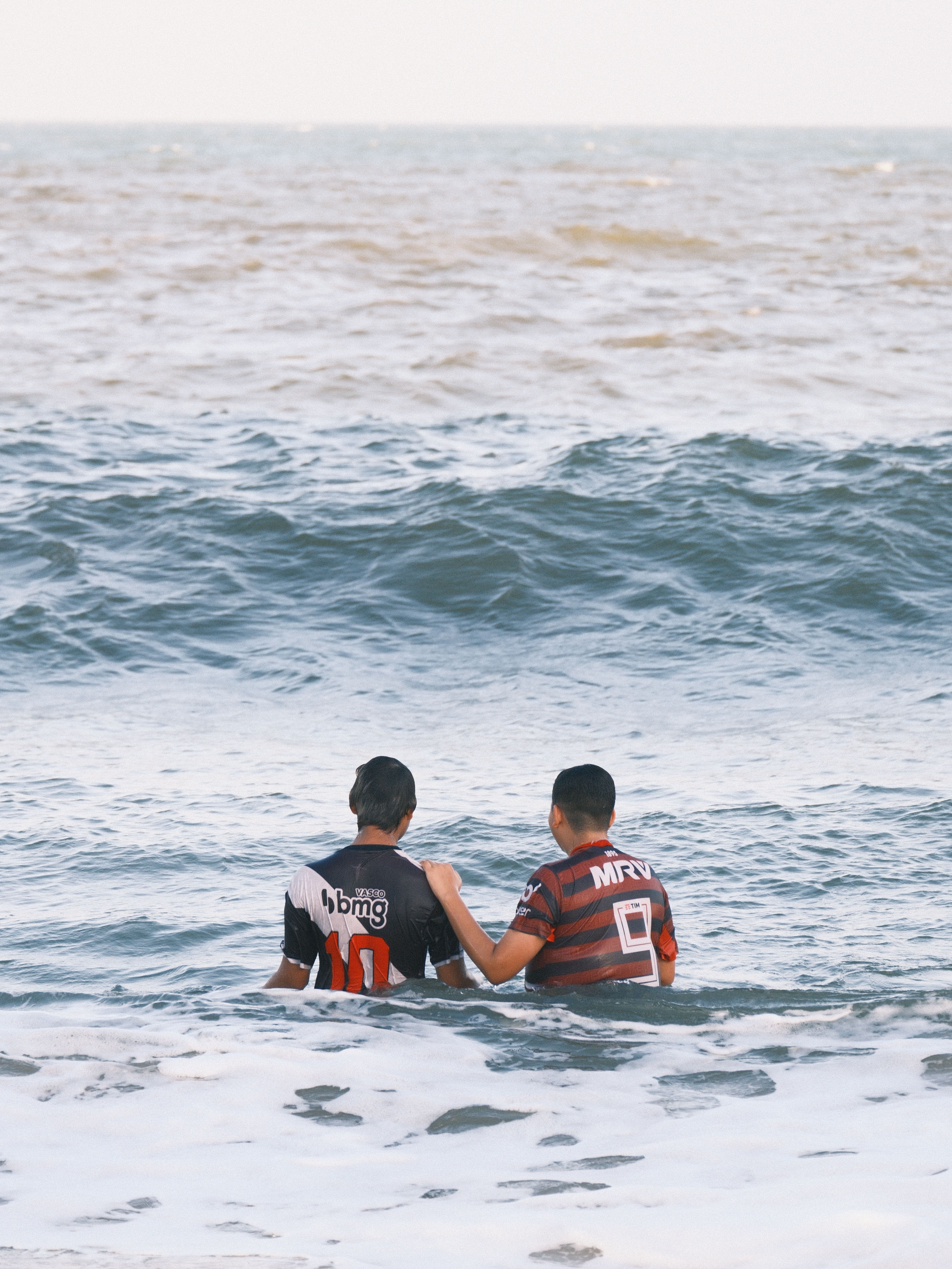 Two boys in soccer jerseys enjoy the ocean, symbolizing friendship and leisure on a sunny day.