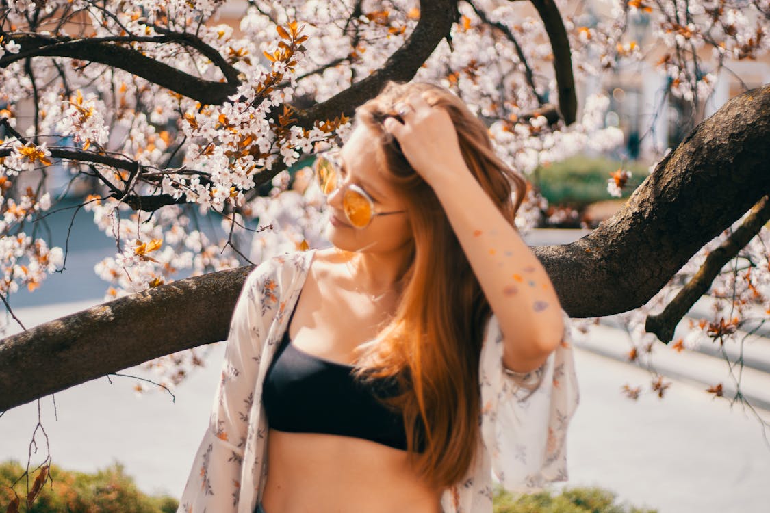 Smiling young woman with long hair wearing black top and blouse enjoying sunshine at bright summer day