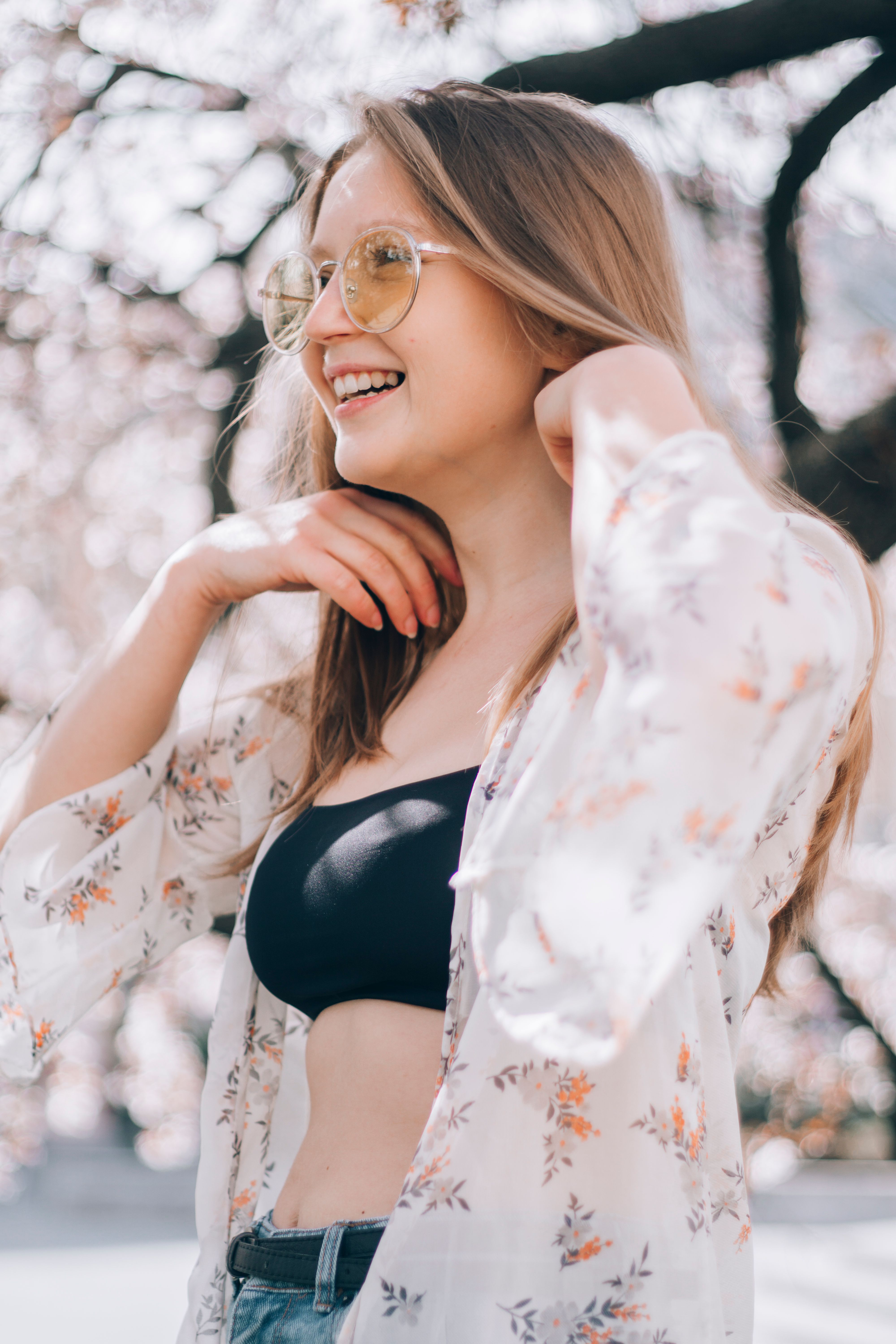 一位穿着上衣和衬衫的开朗年轻女子，站在模糊的树枝上，从低角度笑着