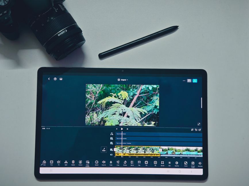 Tablet displaying video editing software with camera and stylus on a white background.