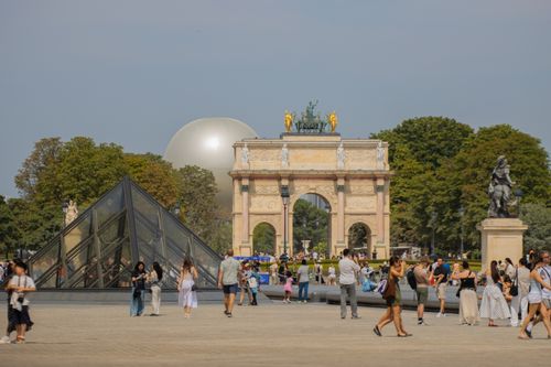 Free Crowds enjoy a sunny day by the Louvre Pyramid and Arc de Triomphe in Paris. Stock Photo