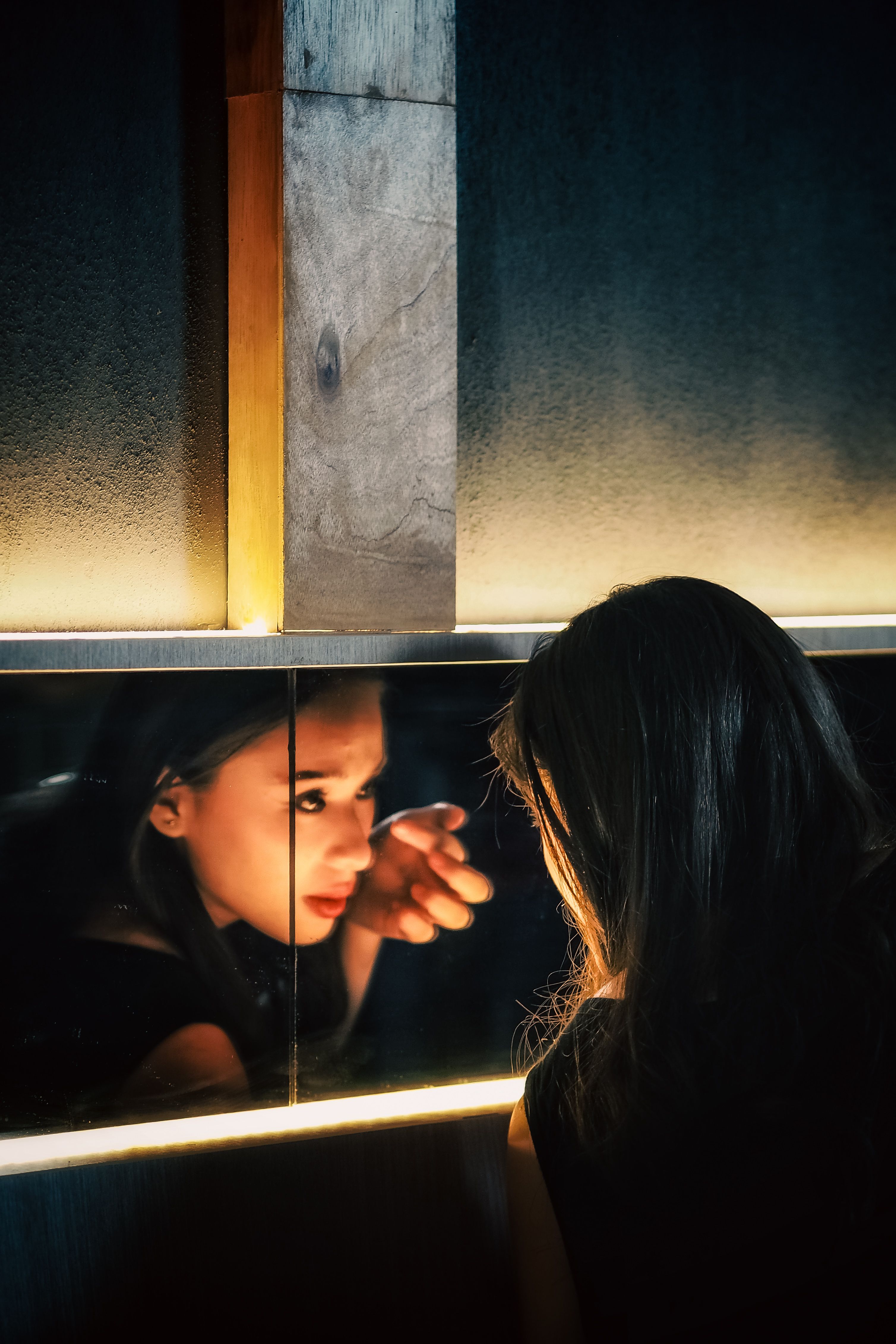 A woman gazes into a mirror with soft lighting, creating an intimate atmosphere.