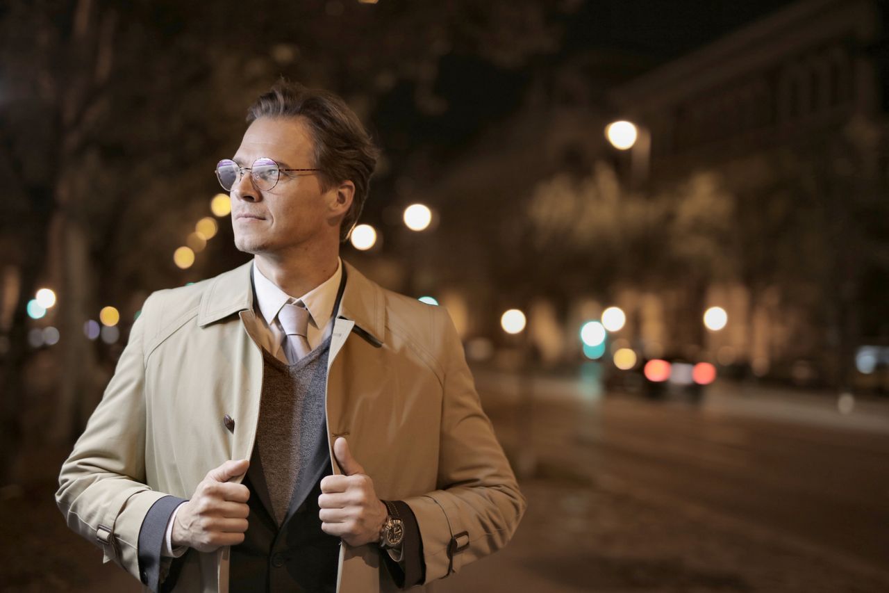 confident adult male in formal wear standing on night street and holdi