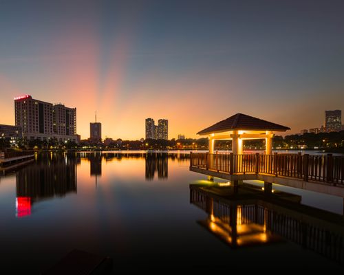 Free Peaceful cityscape at sunset with a glowing gazebo reflected in the calm water, creating a serene urban oasis. Stock Photo