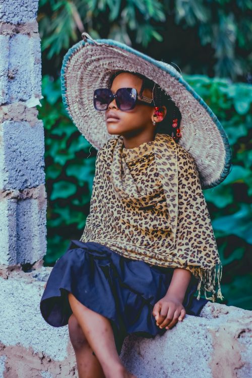 Free Young girl wearing a leopard print scarf, sunglasses, and a wide-brimmed hat outdoors. Stock Photo