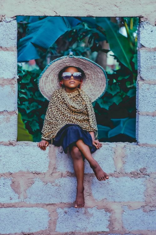 Free A fashionable child wearing sunglasses and a hat, sitting on a wall in Abuja, Nigeria. Stock Photo