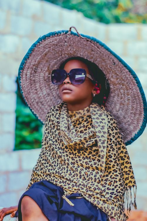 Free A stylish child wearing sunglasses, a large hat, and leopard-print scarf in an outdoor setting. Stock Photo