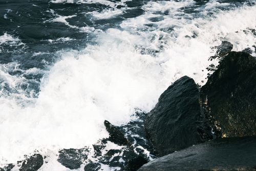 Free Powerful waves crash on dark rocks, capturing the ocean's raw force and beauty. Stock Photo