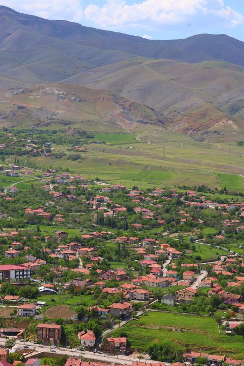 Free Aerial shot of a picturesque village surrounded by lush green fields and rolling hills on a sunny day. Stock Photo