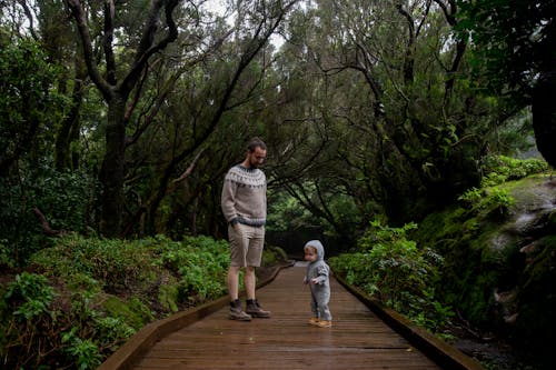 Middle age man in warm sweater with toddler walking on footpath in green forest