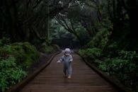 Concentrated kid trying making steps on planked footpath in dark deep forest in cold day