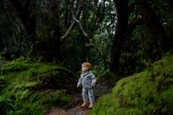 一个好奇的幼儿站在森林小路上，周围绿叶郁郁葱葱