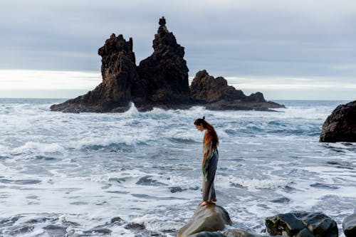 Side view of lonely sad female standing on stone in front of storming ocean