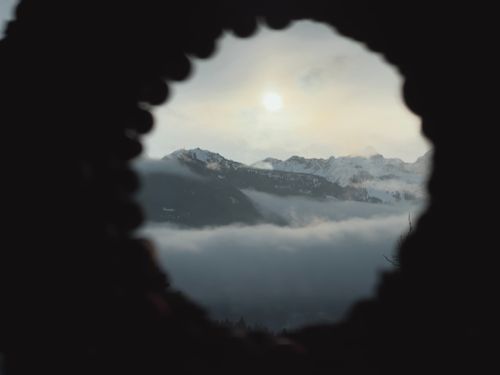 Free View of misty Alpine mountains framed through a natural rock archway at sunrise. Stock Photo