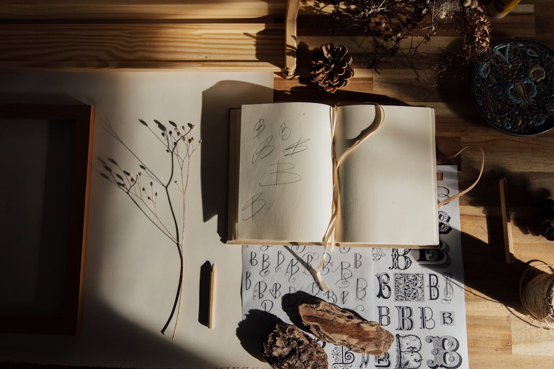 Top view of opened notebook with pencil and dried flower placed on wooden table near other decorative elements illustrating handwriting practice as hobby