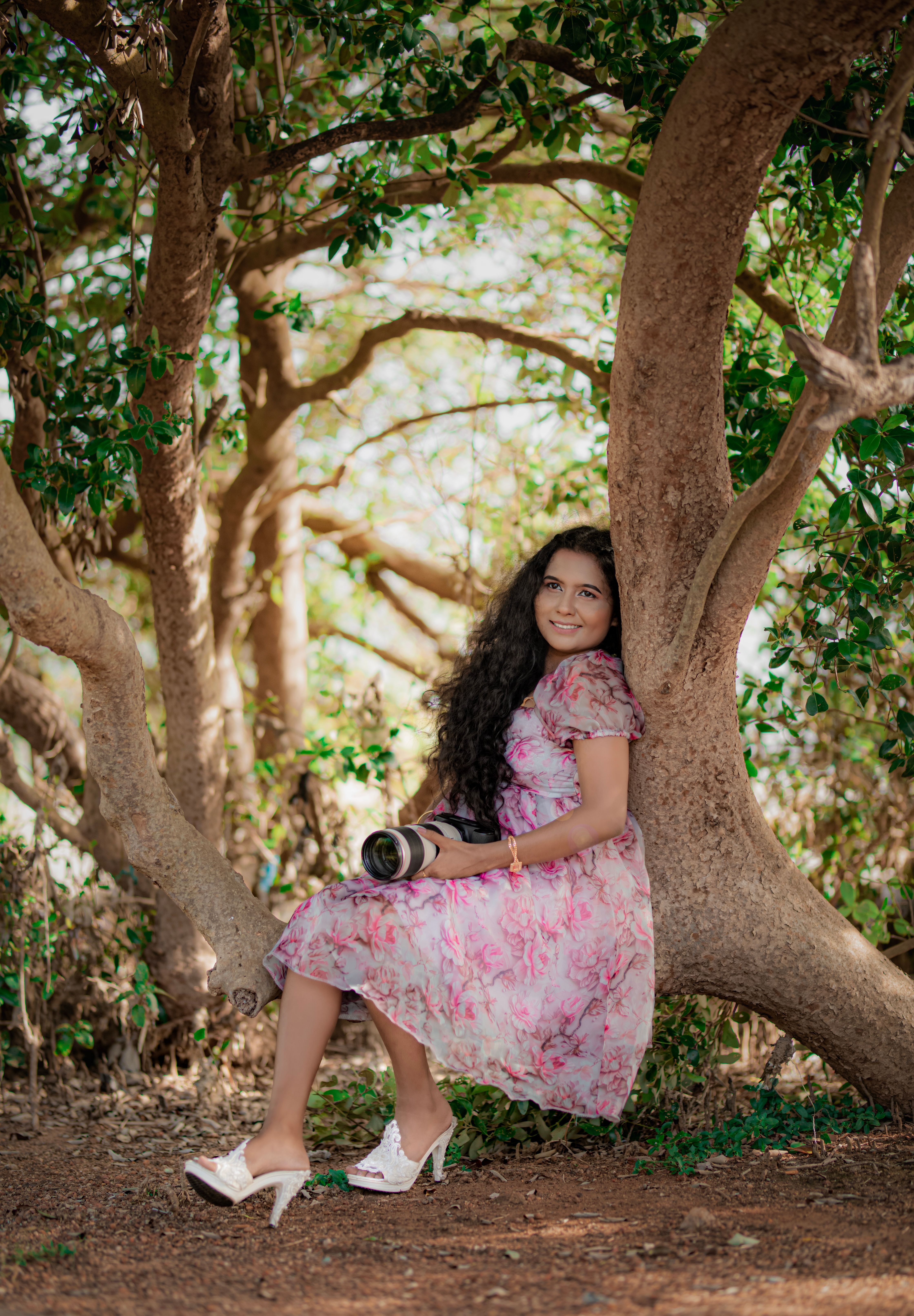 A woman in floral dress holds a camera, sitting under lush trees in Puttalam, Sri Lanka.